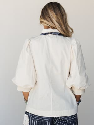 A back-view shot of a cream puff-sleeve blouse with a contrasting navy bandana-print collar, paired with navy striped wide-leg pants — relaxed and expressive with just enough detail to make it interesting.