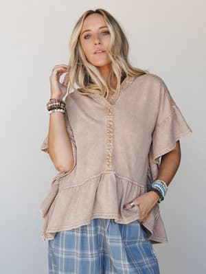 A relaxed peplum hoodie tee in washed almond styled with blue plaid wide-leg pants and stacked bead bracelets — the kind of effortless everyday outfit that looks like you tried just enough.