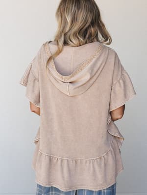 Shot from the back, this mineral-washed hoodie tee in warm almond has a lived-in, effortlessly soft feel — the ruffle trim at the hem and sleeves giving it just enough personality to feel intentional.
