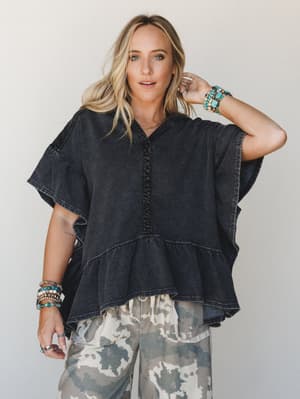 A washed black oversized hoodie tee with tiered ruffle hem and lace trim details, styled with camo wide-leg pants and layered turquoise and beaded bracelets — effortlessly lived-in with a boho edge.