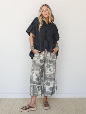 A relaxed, effortlessly cool outfit pairing a washed black oversized hoodie tee with wide-leg camo cropped pants — the kind of look that feels put-together without trying, styled with stacked turquoise bracelets and platform espadrille sandals.