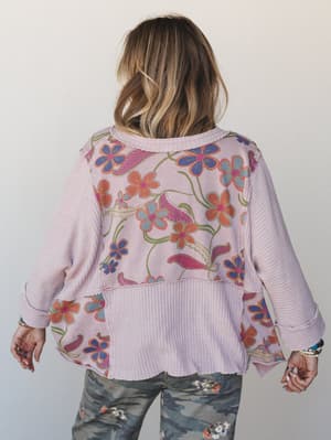 A back-facing shot of a mixed-media pullover top in soft mauve, combining a retro floral print panel with waffle-knit sleeves and hem — the kind of top that looks like it was made from two favorite things sewn together in the best way.