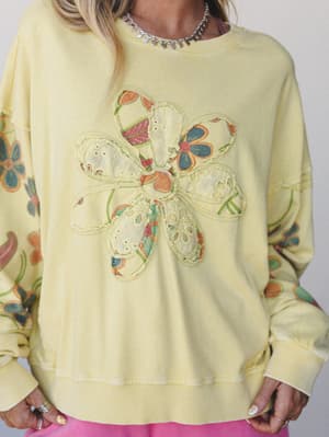 A soft butter-yellow sweatshirt with a mixed-media patchwork flower appliqué on the chest and floral printed sleeves — the kind of piece that feels like it came from someone's cool aunt's vintage collection.
