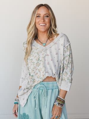 A floral mixed-print pullover top in soft stone grey is styled with mint drawstring pants and stacked beaded bracelets — the kind of effortless, happy outfit that feels like a good mood in clothing form.