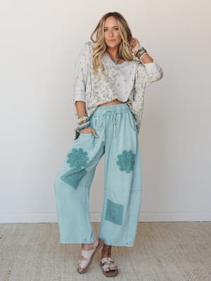 A relaxed, put-together look built around wide-leg mint pants with crochet floral appliqués, paired with a ditsy floral sweatshirt tied at the hem — the kind of outfit that feels effortless but clearly thought through.