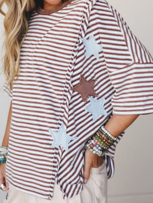 A relaxed oversized striped top in espresso and white gets a playful, personality-forward moment with mixed star appliqués running down the front — styled with stacked beaded bracelets and cream wide-leg pants for that effortless, wearable serotonin