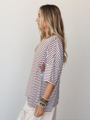 A relaxed striped top with star appliqué patches worn in a side profile shot — the kind of top that feels effortless stacked with beaded bracelets and drawstring pants.