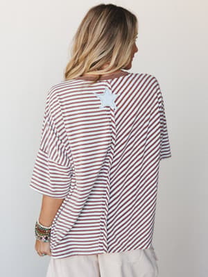 A relaxed striped top shot from the back, showing off a mixed-direction stripe pattern and a worn-in star patch detail — the kind of top that looks like it's been loved for years and somehow still pulls everything together.