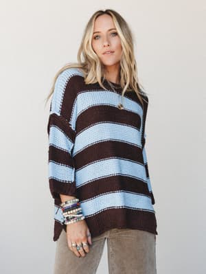 An oversized striped knit sweater in mocha and sky blue, styled with wide-leg corduroy pants and a stack of beaded bracelets — the kind of laid-back, put-together look that feels like a Saturday done right.