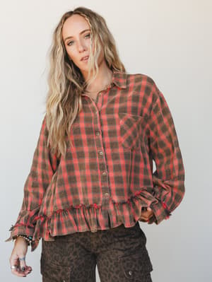 A relaxed plaid flannel top with ruffle hem and frayed trim details, styled with leopard print cargo pants and layered jewelry — the kind of outfit that looks like it just happened and somehow works perfectly.