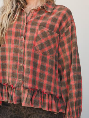 A close-up of a plaid flannel button-down with an unexpected ruffle hem — the kind of top that feels like a flannel shirt went to a barn dance and never looked back.