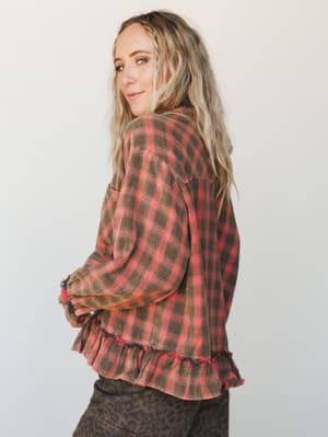 A relaxed plaid flannel top with a ruffled hem and volume sleeves photographed from the back three-quarter angle — the kind of piece that makes a leopard-print pant look like a totally reasonable decision.