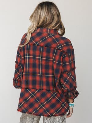 Shot from behind, this plaid flannel shacket in deep red and navy has that lived-in, slightly undone quality — raw frayed edges at the seams and hem, stacked bracelets peeking out at the wrist, worn over a snakeskin-print bottom for a little unexpect