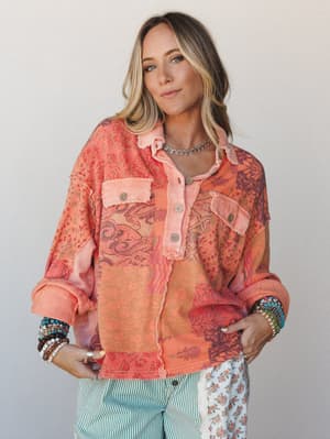 A patchwork oversized blouse in warm tangerine and plum tones worn with mixed-print pants and stacked boho bracelets — the kind of top that does all the talking.