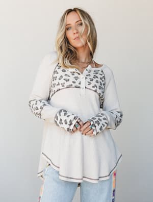 A relaxed waffle-knit henley top in cream with leopard print contrast panels on the yoke and sleeves, styled with light wash floral-trim jeans and layered jewelry for an effortlessly personal, everyday-boho feel.