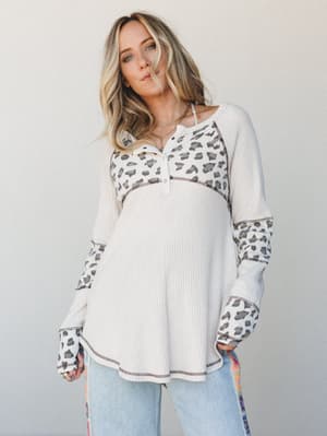 A relaxed waffle-knit henley top in cream with leopard print contrast panels at the chest and sleeves, styled with light wash jeans — the kind of top that makes a regular Tuesday feel a little more like you.