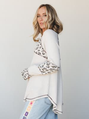 A relaxed waffle-knit top in cream with leopard print contrast panels at the shoulders and cuffs, paired with light wash jeans featuring floral embroidery down the side — the kind of effortless mix-and-match that looks like you meant to do it.