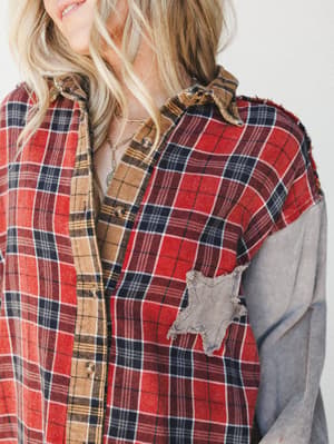 A close-up of a patchwork flannel button-down with mixed plaid panels in red, tan, and navy paired with a washed gray corduroy sleeve — the kind of shirt that looks like it was loved into existence.