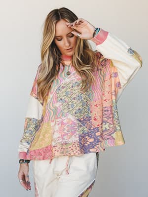 A relaxed, oversized patchwork top in a dreamy mix of pastels — worn with cream joggers and layered jewelry, the whole look feels like a mood board come to life.