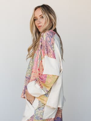 A model shot from a three-quarter back angle showing an oversized patchwork top with a mix of boho prints — the kind of piece that looks like it was assembled from the most beautiful vintage scarves you've ever found.