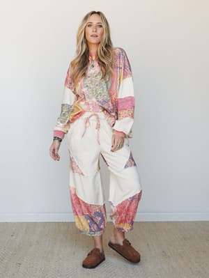 A relaxed, full-body shot of a model wearing a mixed patchwork print matching set — an oversized sweatshirt top and wide-leg jogger pants — styled with brown suede clogs and layered jewelry for an easy, expressive boho-casual look.
