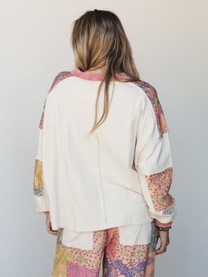 Shot from the back, this oversized cream sweatshirt-style top features patchwork floral and paisley fabric panels along the sleeves and sides, paired with matching patchwork wide-leg pants — the whole look has that collected, one-of-a-kind energy.