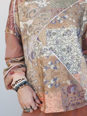 A close-up torso shot of a mixed patchwork floral and paisley top in warm mocha tones, styled with layered beaded bracelets and stacked rings for that collected, lived-in boho feel.
