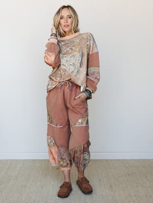 A relaxed patchwork matching set — mixed-print sweatshirt top and drawstring jogger pants in warm mocha and blush tones, styled with stacked beaded bracelets and suede clogs for an effortlessly lived-in boho look.
