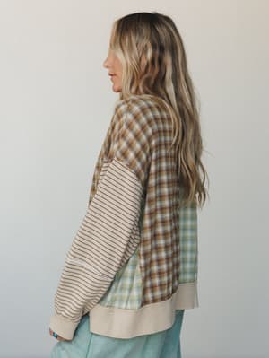 A mixed-media long sleeve top shot from behind — the kind of piece that looks like it was made from your favorite flannels, with patchwork plaid panels and a striped sleeve that somehow all work together in the best worn-in way.