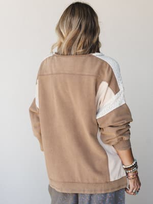 A relaxed oversized sweatshirt shot from the back, showing a warm mocha and blush colorblock body with a crochet lace shoulder stripe detail — the kind of top that makes a Saturday feel intentional.