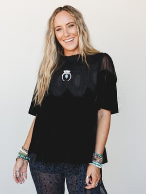 A relaxed black velvet top with lace overlay detail and sheer mesh sleeves, styled with stacked turquoise bracelets and a silver crescent necklace — the kind of outfit that feels effortlessly dressed up without trying too hard.