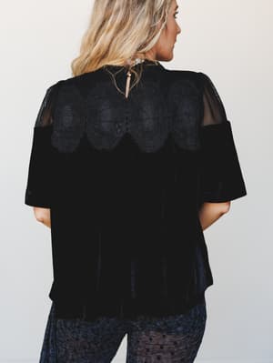 Shot from the back, this black velvet top reveals its best detail — a scalloped lace yoke and sheer mesh shoulders that give it a moody, romantic edge, paired with polka dot wide-leg pants for a full tonal look.