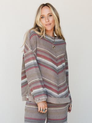 A relaxed waffle-knit pullover in earthy multi-stripe layers up effortlessly as a matching set, styled with layered gold necklaces and stacked turquoise rings for that lived-in boho feel.