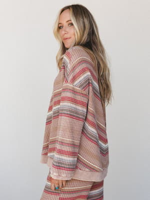 A relaxed striped waffle-knit pullover shot in profile against a soft studio backdrop — the kind of top that looks equally at home on a slow Sunday morning or a casual coffee run, styled with matching bottoms and layered rings for that effortless, li