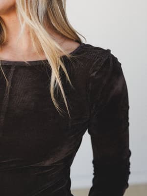 A close-up detail shot of a soft, dark charcoal long-sleeve top with subtle ruching along the shoulder and sleeve — understated and wearable, the kind of piece that does more than it lets on.