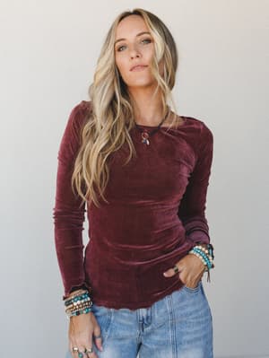A velvet long-sleeve top in deep mulberry pairs effortlessly with light-wash jeans, styled with stacked beaded bracelets and a dainty charm necklace — the kind of outfit that feels pulled-together without trying.