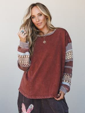 A relaxed mixed-media pullover in washed mocha with Fair Isle and stripe-knit sleeves, styled with dark corduroys and layered silver jewelry — the kind of top that looks like it was meant to be worn on a slow weekend morning.