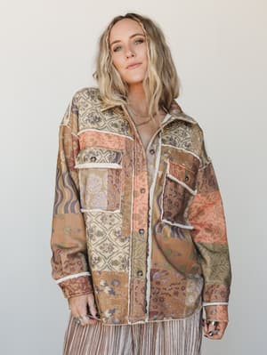 A relaxed patchwork shacket in warm earthy tones worn open over a striped skirt — the kind of piece that looks like it's been loved for years and somehow gets better every time you reach for it.