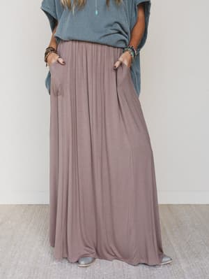 Person wearing a long, flowing skirt and a blue top against a plain background
