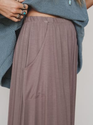 Close-up of a person wearing a blue sweater and brown pleated skirt on a plain background