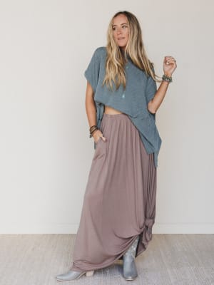 Woman wearing a blue top and long mauve skirt against a plain background