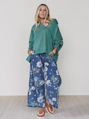 Green / Woman wearing a teal hoodie and blue floral pants on a white background