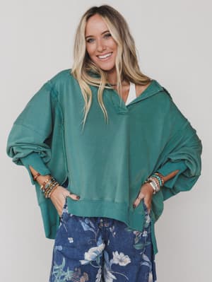 Green / Woman wearing a teal oversized sweater with floral pants against a plain background