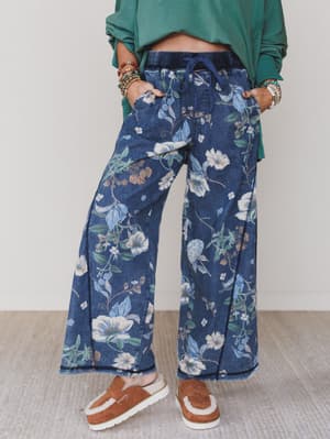 Green / Person wearing blue floral pants with a green top and brown shoes on a light background