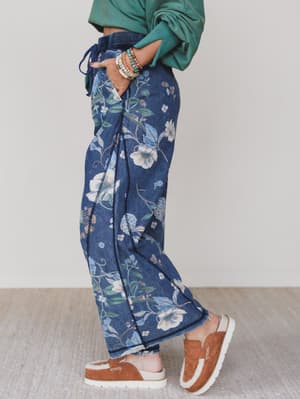 Green / Person wearing blue floral pants with a green top and brown shoes on a light background