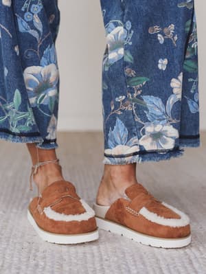 Green / Brown suede shoes with white fur trim worn with blue floral pants on a neutral background