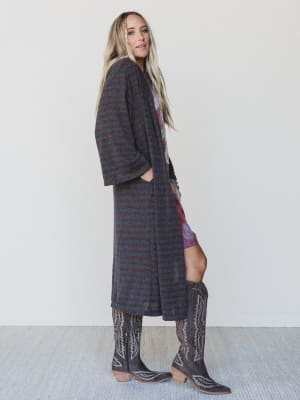 Woman wearing a long striped coat, patterned dress, and cowboy boots on a white background