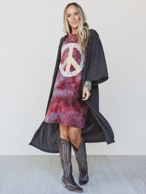 Woman wearing a tie-dye dress with a peace symbol and a dark poncho against a white background