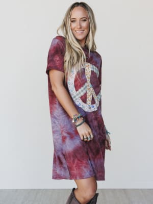 Woman wearing a tie-dye dress with a peace sign design on a plain background