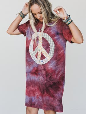 Person wearing a tie-dye dress with a peace symbol design on a plain background